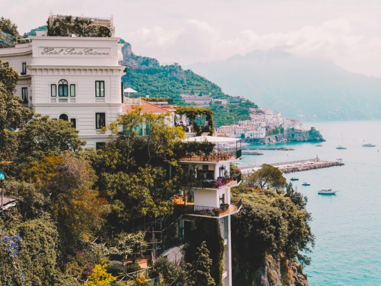 Stunning view of Amalfi Coast with cliffs, buildings, and boats. Perfect for luxury travel and architecture lovers, by Duchess Concept